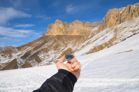 A mans hand holds a pocket magnetic compass for navigation against the backdrop of a rocky slope and a mountain. The concept of finding a way. Gaining freedom. freedom of choiceの写真素材