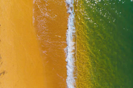 Top view of a deserted coast of golden sand and turquoise green clear sea with waves and foam. Aerial viewの写真素材