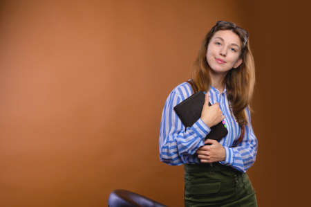 Portrait of a friendly positive Caucasian young woman dressed in corporate formal dress with a notepad in her hands. Smiling looks into the camera. Studio portraitの写真素材