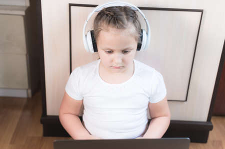 Girl Little child in headphones uses a laptop intently while sitting on the floor in her roomの写真素材