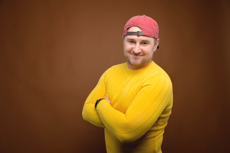 Portrait of an attractive friendly Caucasian man in a cap and yellow sweater on a brown background....