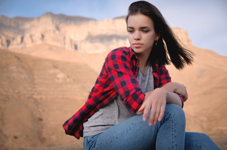 Attractive cute young caucasian woman sitting on stones in the mountains against the backdrop of...