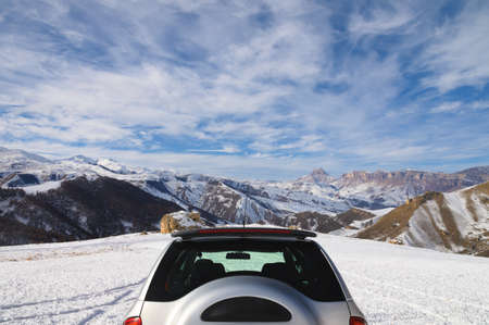 Rear view of the unrecognizable upper part of an SUV high in the mountains in winter against the backdrop of snow-capped rocks on a sunny dayの写真素材