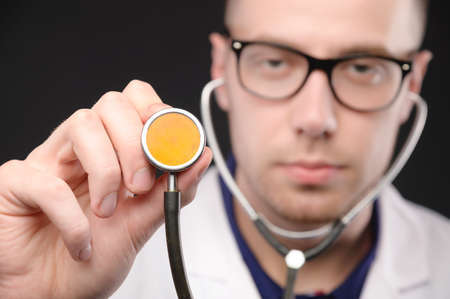 A young doctor or nurse holding a stethoscope disc, pointing at the camera, getting ready to listen to the patients heartbeat and lungs. Focus on stethoscope discの写真素材