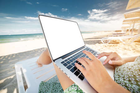 young woman freelancer sits on a sun lounger with a laptop on the seashoreの写真素材