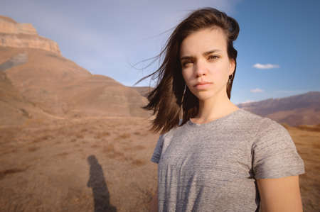 young attractive woman stands in a t-shirt against a background of mountains