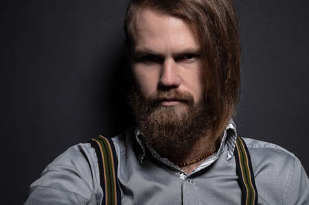 Portrait of a bearded man with an intense look standing in a dark room against a black background