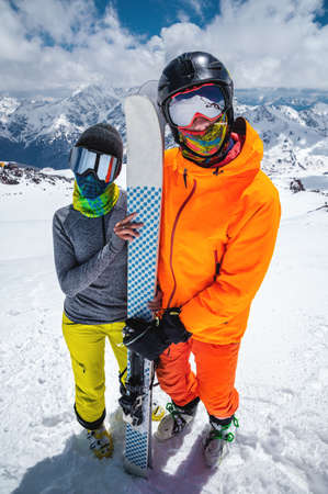 Portrait of a pair of young skiers athletes man and woman in ski masks with skis stand and look at...