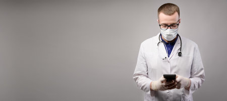panoramic background for text, young male doctor in uniform looks at the phone, studio shotの写真素材