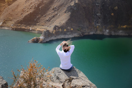 Attractive cute young caucasian woman sitting on stones in the mountains against the background of a...