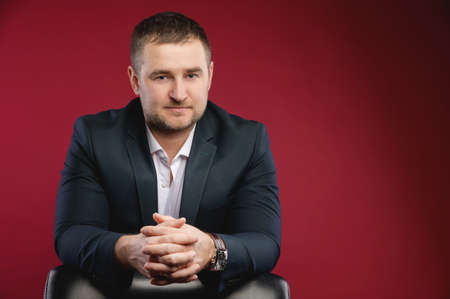 Business portrait of an attractive middle-aged man with stubble on his face in a black suit. Studio photo. The boss sits and looks at the cameraの写真素材