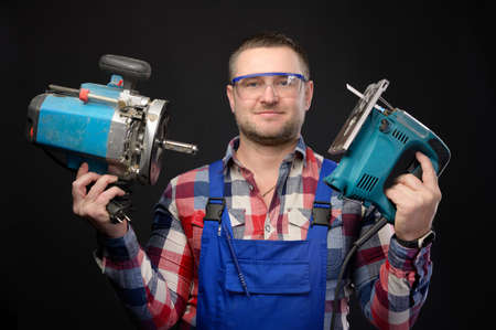 Caucasian repairman in goggles holding woodworking tools. Carpenter portrait on black studio...