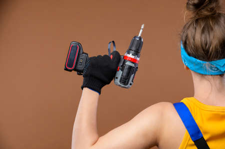 Back view energetic strong young Caucasian woman in a work uniform and goggles shows that she is...