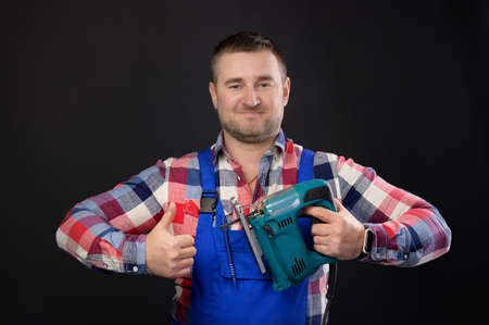 Caucasian male repairman in glasses with woodworking tools in hand shows thumb up. Portrait of a...