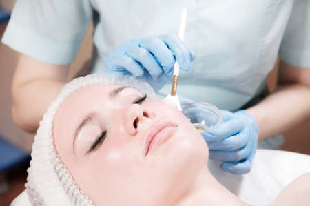 face of a young woman close-up lying down cosmetic procedure is performed applying a rejuvenating...