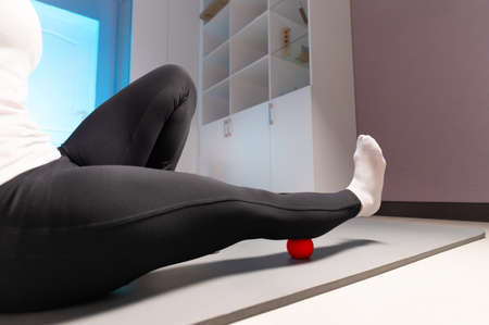 Close-up of self-massage of a sports woman indoors using a massage ball. Myofascial massage without...