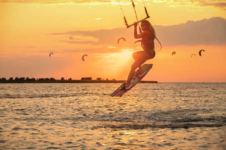 Young woman professional kiter performs a difficult trick in the air on a beautiful background of the sunset and seaの写真素材