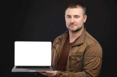 Portrait of casual friendly Caucasian man holding laptop with cut out screen. Laptop presentation. Studio portraitの写真素材