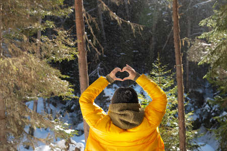 Back portrait young caucasian woman and shows fingers gesture of heart, love at eye level. Back view in forestの写真素材