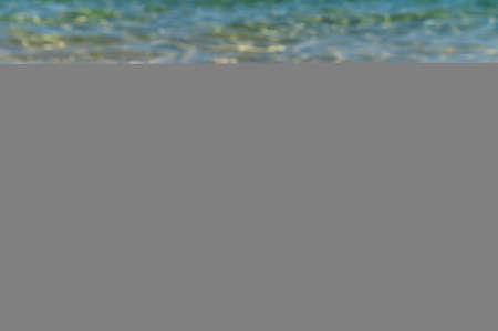 Snorkeling equipment on the sand with ocean waves splashing the water. Black fins, black mask, snorkel on sandy texture background. Items lying in the sandの写真素材