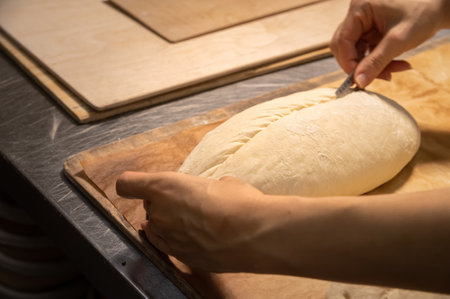 Close-up of a bakers female hands cutting a loaf of dough into a loaf of bread with a blade before baking in the oven. Craft craft bread productionの写真素材