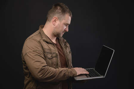 Middle aged Caucasian man uses laptop while standing in studio. Portrait of a freelancer surfing the...