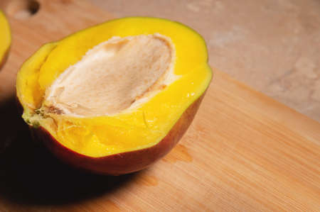 Cut a very ripe mango in half on a cutting board in your home kitchen. Yellow juicy tasty mango....
