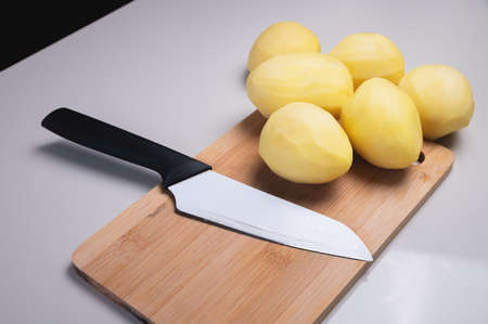 Peeled potatoes on a wooden cutting board next to a kitchen knife. Home cooking vegetables. Healthy foodの写真素材