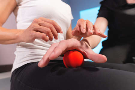 Close-up of a male massage therapist showing a client how to use and massage a ball. Myofascial thigh massageの写真素材
