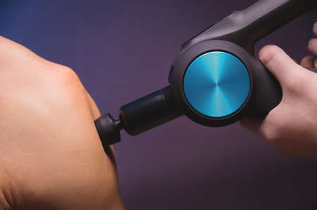 Shoulder massage with a percussion massager in a professional massage parlour. Working as a percussion massager in a dark roomの写真素材