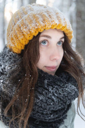 portrait of a smiling young caucasian woman in a bright woolen hat and scarf, against the backdrop of a snowy forest.の写真素材