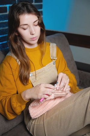 cute young caucasian woman sitting on sofa at home and crocheting wool product
