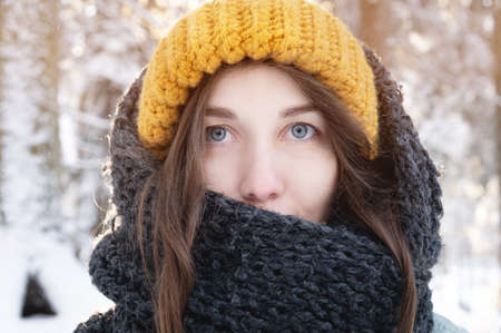 portrait of a smiling young caucasian woman in a bright woolen hat and scarf, against the backdrop...