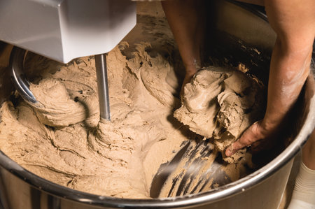 Close-up of bakers female hands holding dough against the background of a production dough mixer in a bakeryの写真素材