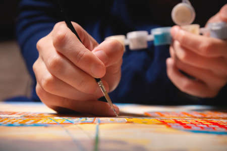 Close-up of a female artists hand painting with watercolors color on canvas with a brush in a dark...