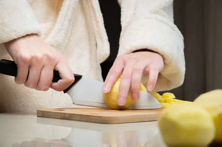 young caucasian woman in a bathrobe stands and cuts potatoes on a cutting board