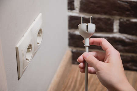 A female hand inserts white electric plug into a euro-format socket close-upの写真素材