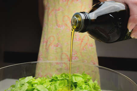 close-up of young woman dressing vegetable salad with olive oil at homeの写真素材