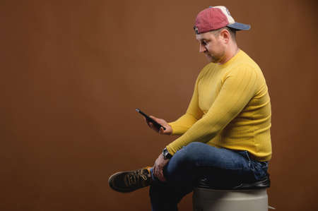 Chubby caucasian businessman sitting uses smart mobile phone while looking at camera. Studio...