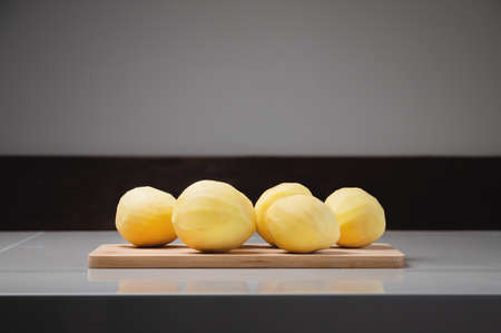 Close-up Several peeled potatoes on a wooden cutting board on a white table.の写真素材