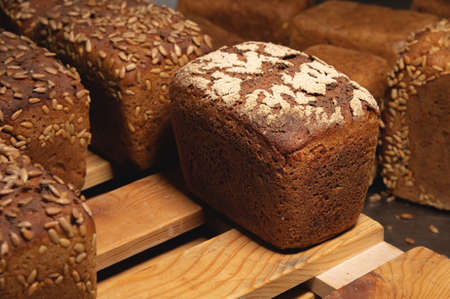 Close-up rye loaves of hot rye bread stand on a wooden tray in a dark bakery room
