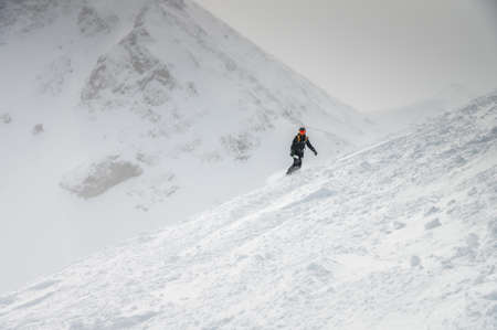 Young sportswoman snowboarder ride on a snowy slope against the backdrop of mountains on a winter...