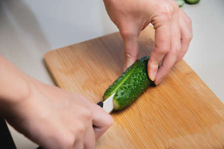 Close-up of female hands cutting fresh cucumber on cutting board at home kitchenの写真素材