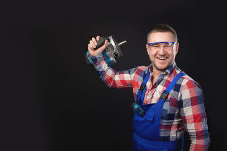 Portrait of an attractive repairman in uniform and plaid shirt with stubble on his face,...