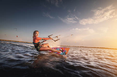 Water sports. The girl is engaged in kitesurfing with a kite in the sky on board in the blue sea, riding the waves with water splashes. Recreational activities,の写真素材