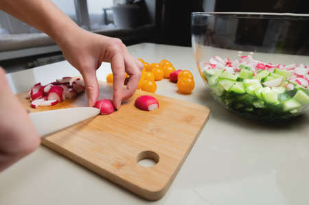 Close-up of female hands cutting fresh radish on cutting board at home kitchen
