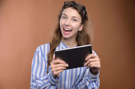 Portrait of a cheerful charming girl holding a digital tablet with a toothy smile, wearing a shirt...