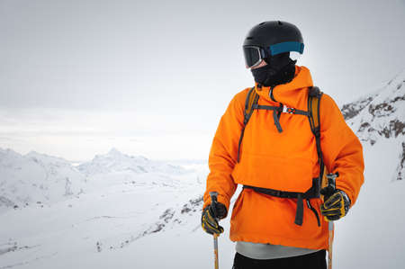 Portrait of a male skier at the top against the backdrop of epic mountains in the clouds.