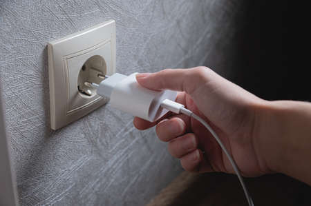 A young woman inserts a plug into a socket. A young woman plugs a charger or electrical appliance power cord into a socket. High quality photoの写真素材