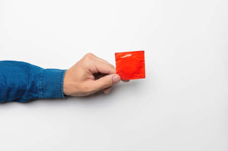 A mans hand holds a red condom in a package on a white background. High definition product. Close-up. Contraceptionの写真素材